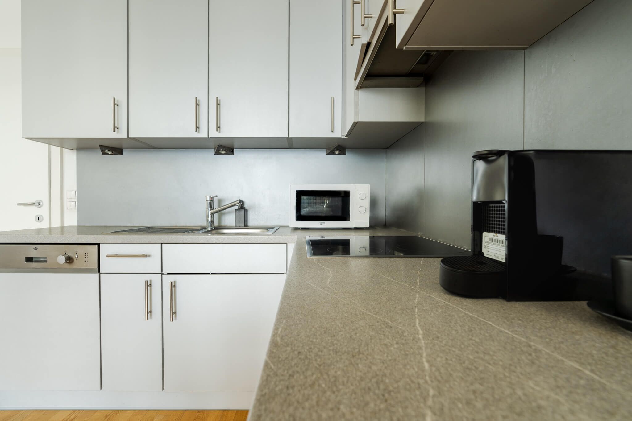Una cucina moderna con mobili bianchi, un forno a microonde, una macchina per il caffè e una lavastoviglie.