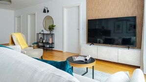 A modern living room with a large flat-screen TV, a sofa, a coffee table, and a chair. - Business & Family Ambiente Apartments (Bratislava)