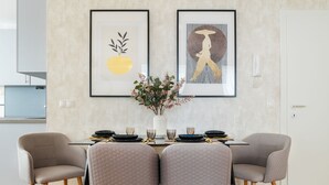 A dining area with a table set for two, framed artwork on the wall, and a vase with flowers. - Business & Family Ambiente Apartments (Bratislava)