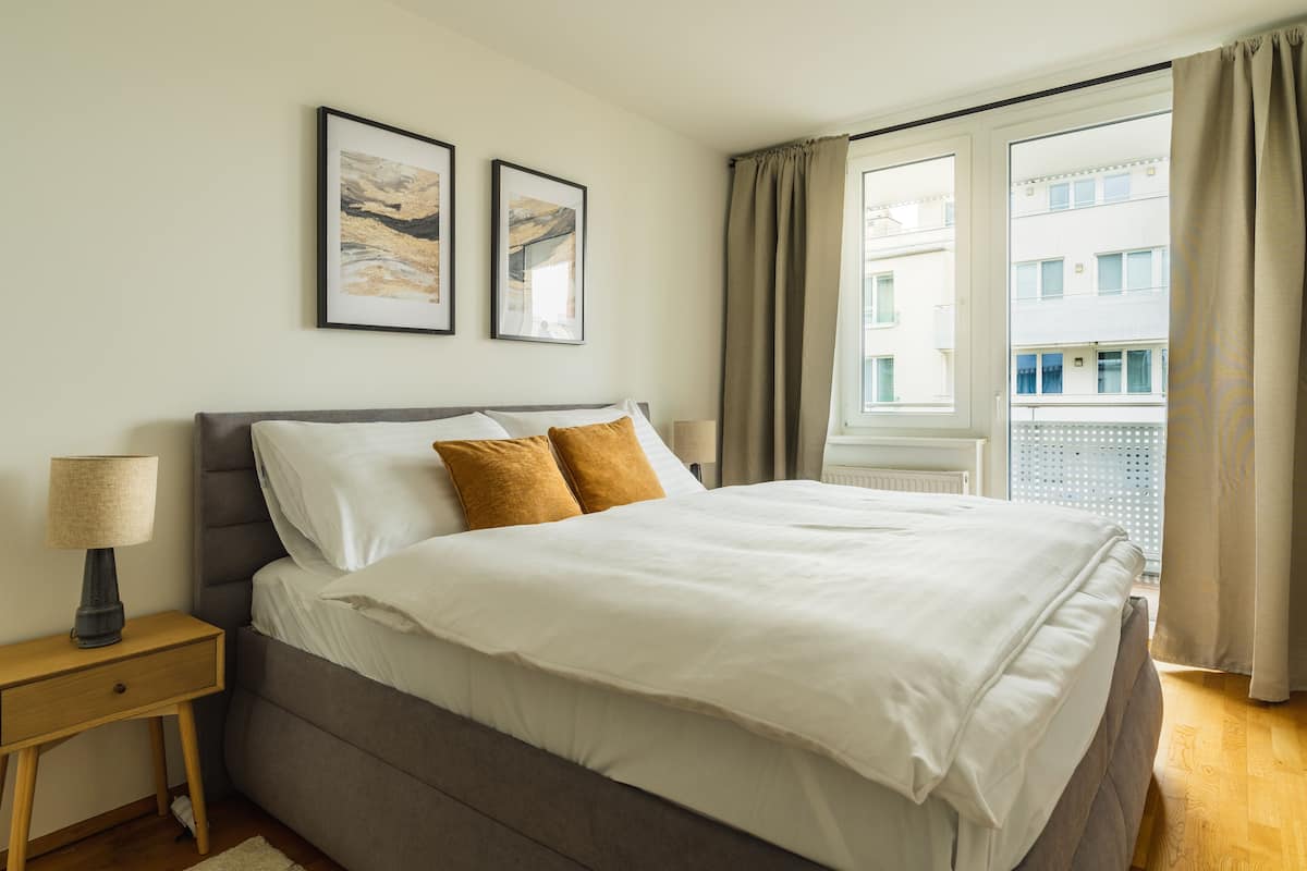 A neatly made bed with a grey headboard, white bedding, and two brown pillows. There are two framed pictures on the wall above the bed.