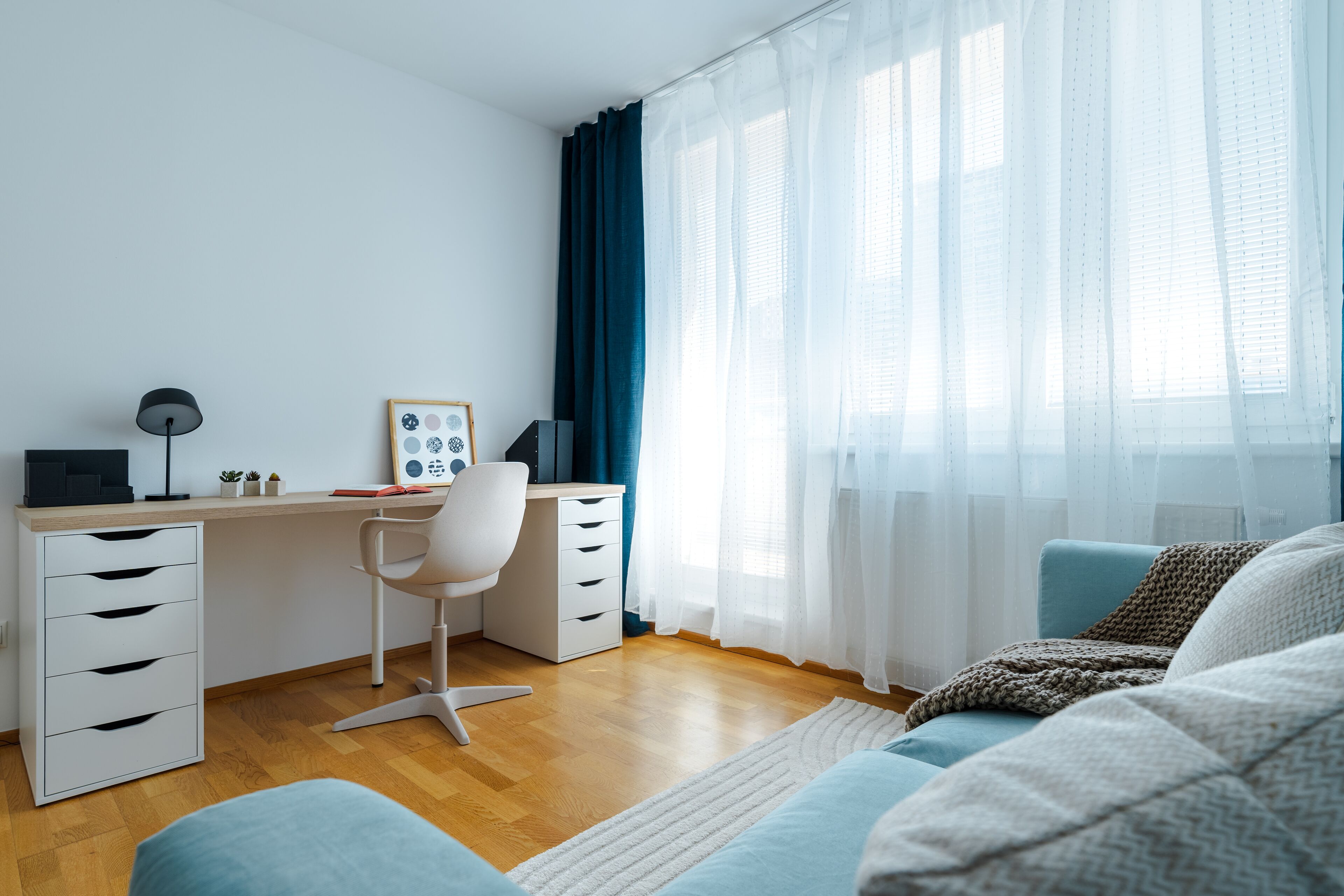 A modern bedroom with a wooden desk, white chair, and a bed with a blue and white color scheme.