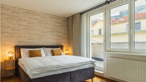 A bedroom with a large bed, two bedside lamps, a view of buildings outside, and a radiator on the wall. - Business & Family Ambiente Apartments (Bratislava)