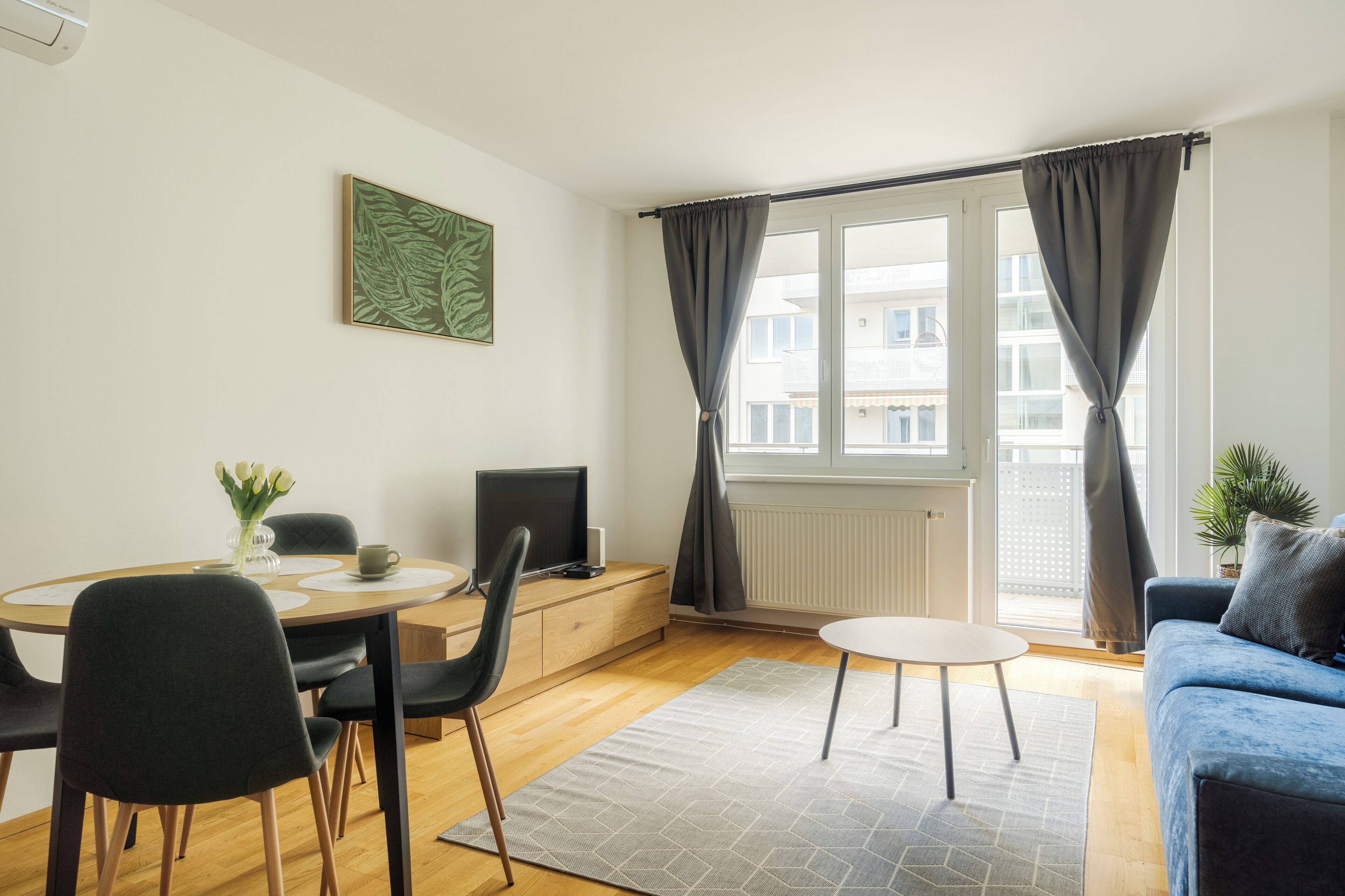 Ett modernt vardagsrum med en matplats, en soffa, en tv och ett fönster med gardiner.