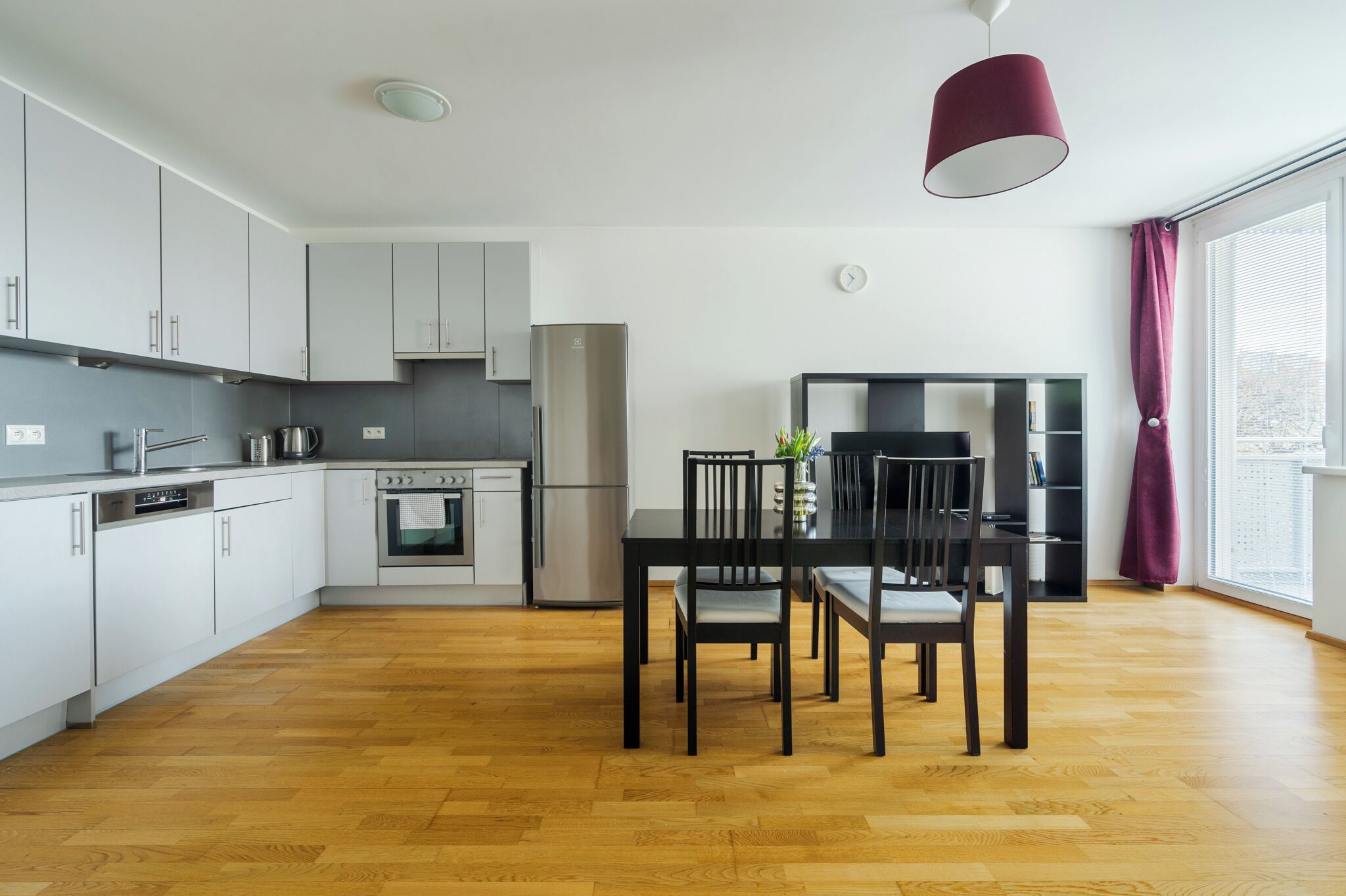 A modern kitchen with white cabinets, a stainless steel refrigerator, and a dining area with a black table and chairs.
