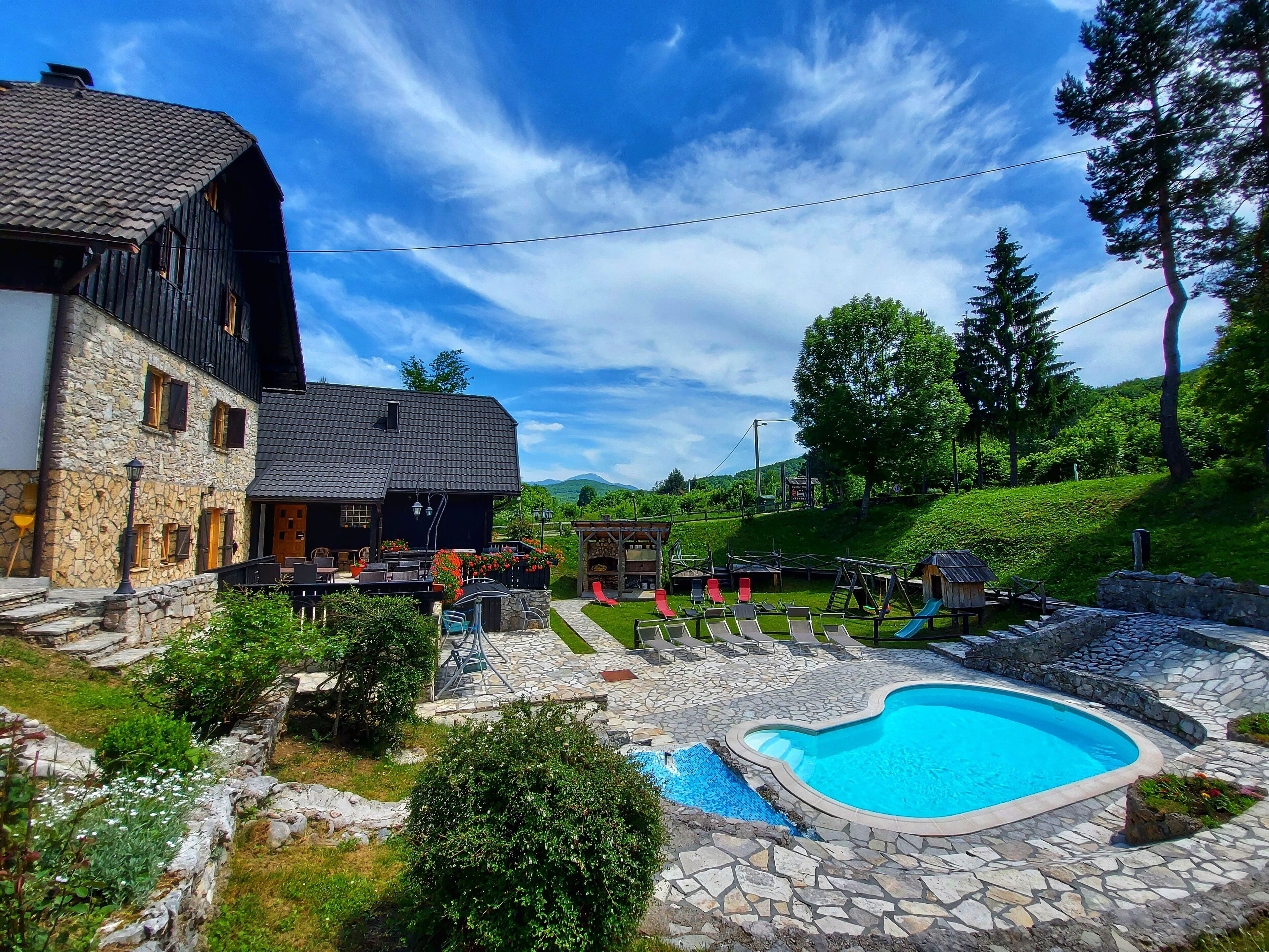 A stone building with a pool, outdoor seating, and a playground.