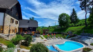 A stone building with a pool, outdoor seating, and a playground.