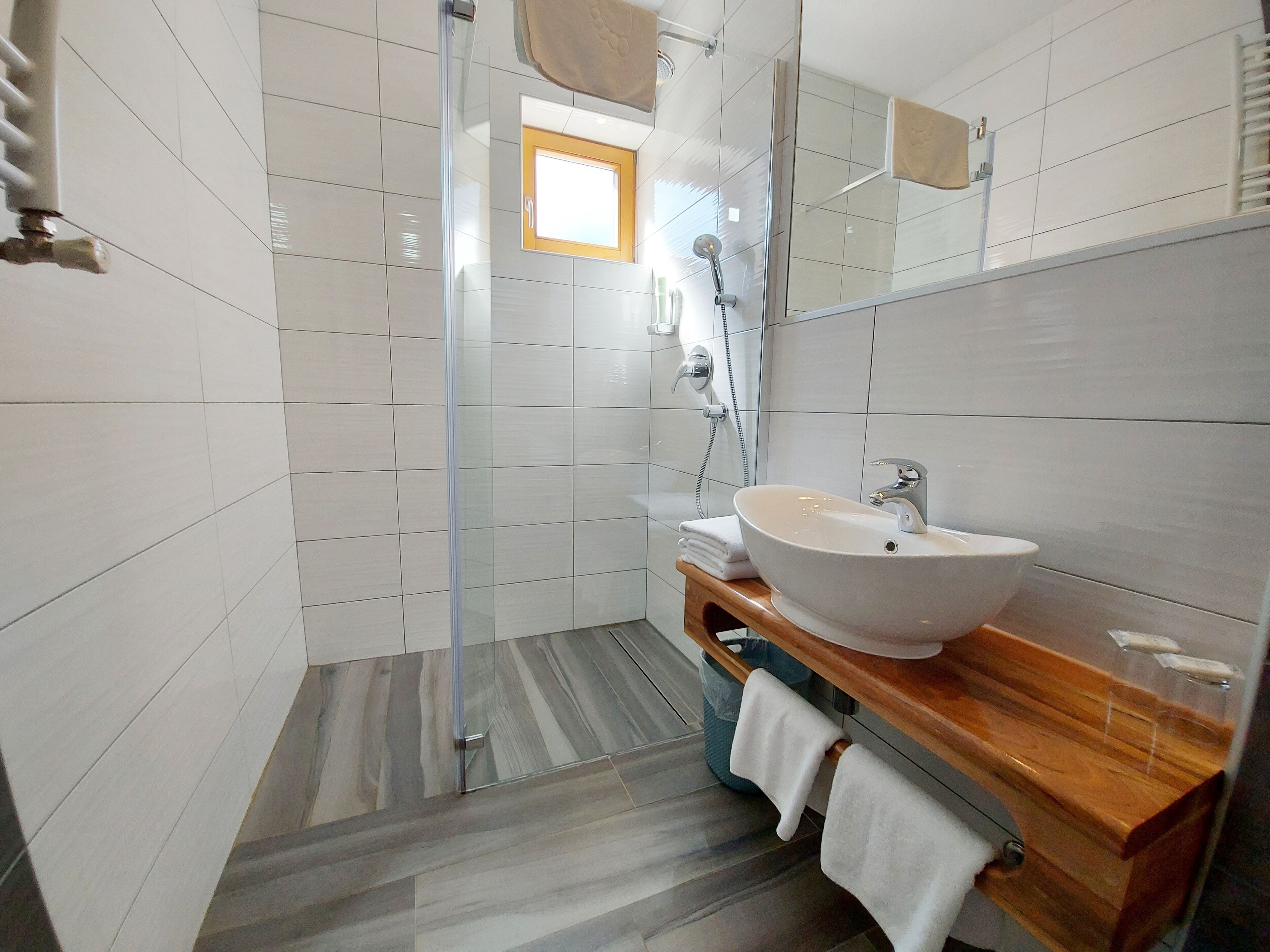 A modern bathroom with a glass shower enclosure, a white sink, and a wooden vanity.