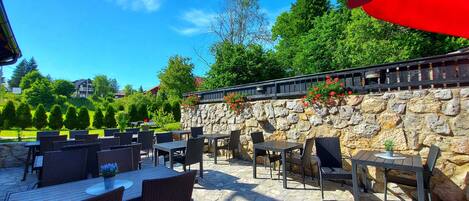 An outdoor patio with stone flooring, wicker furniture, and a stone wall with red flowers.