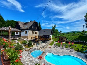 A two-story house with a stone facade, a swimming pool, and a garden with red flowers. - Plitvice Etno House (Plitvicka Jezera)