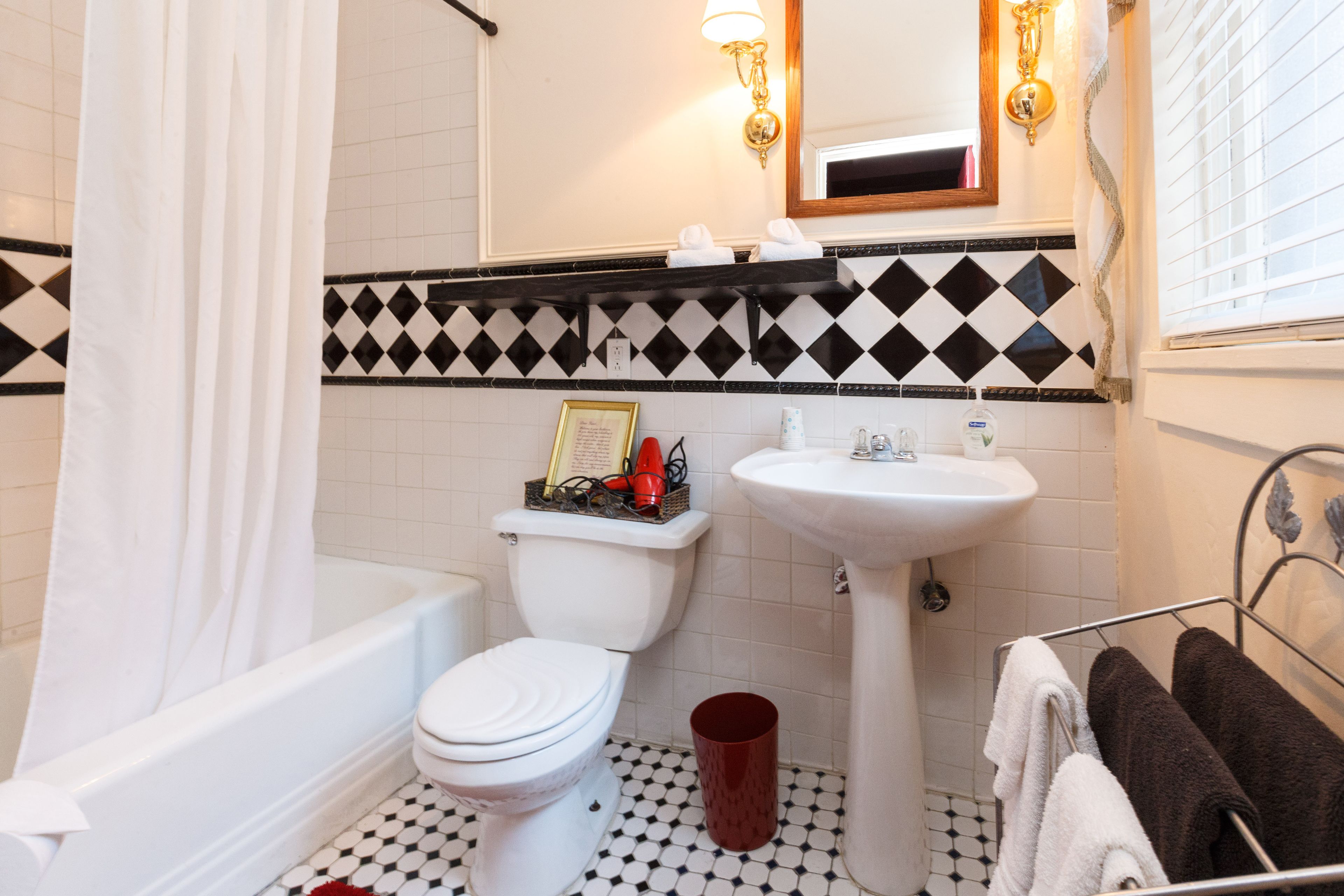 Un baño con inodoro blanco, lavamanos y bañera. Hay un balde rojo en el suelo.