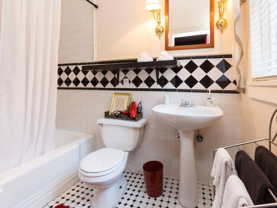 Ein Badezimmer mit Toilette, Waschbecken und Badewanne. Auf dem Boden steht ein roter Eimer.