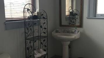 Un baño con inodoro, lavamanos, espejo y un perchero metálico con toallas.