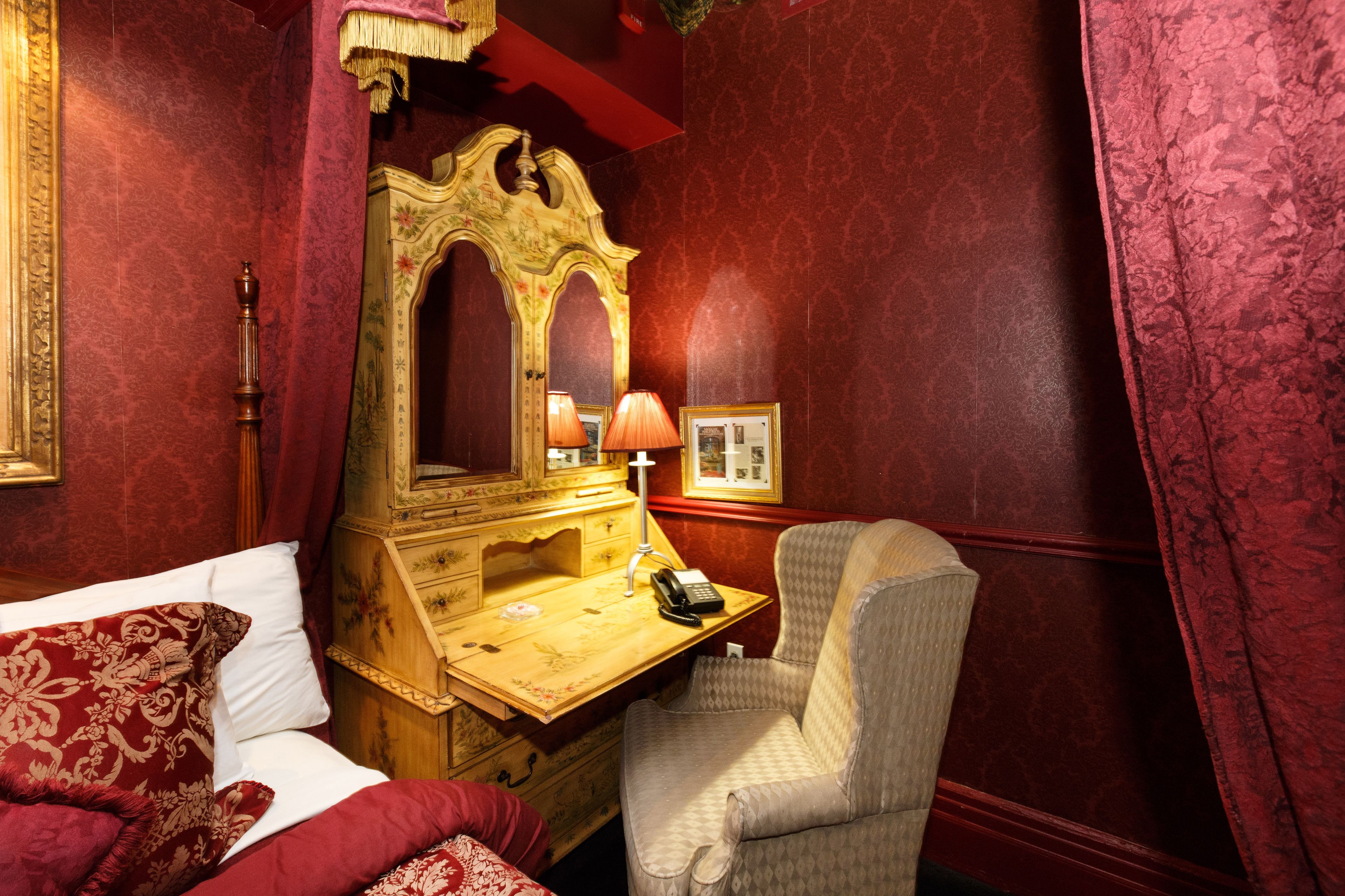 A room with a bed, a wooden desk with a telephone, a chair, and a large mirror.