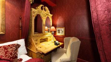A room with a bed, a wooden desk with a telephone, a chair, and a large mirror.