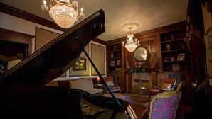 A grand piano in a cozy living room with a chandelier, wooden bookshelves, and a fireplace. - Boggs Mansion (Pittsburgh)