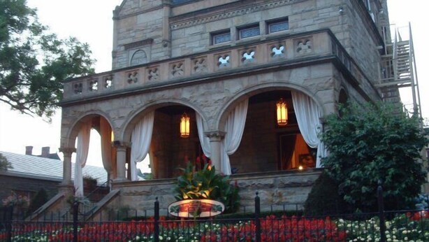 A stone building with a steep roof, arched windows, and a balcony with draped curtains. - Boggs Mansion (Pittsburgh)