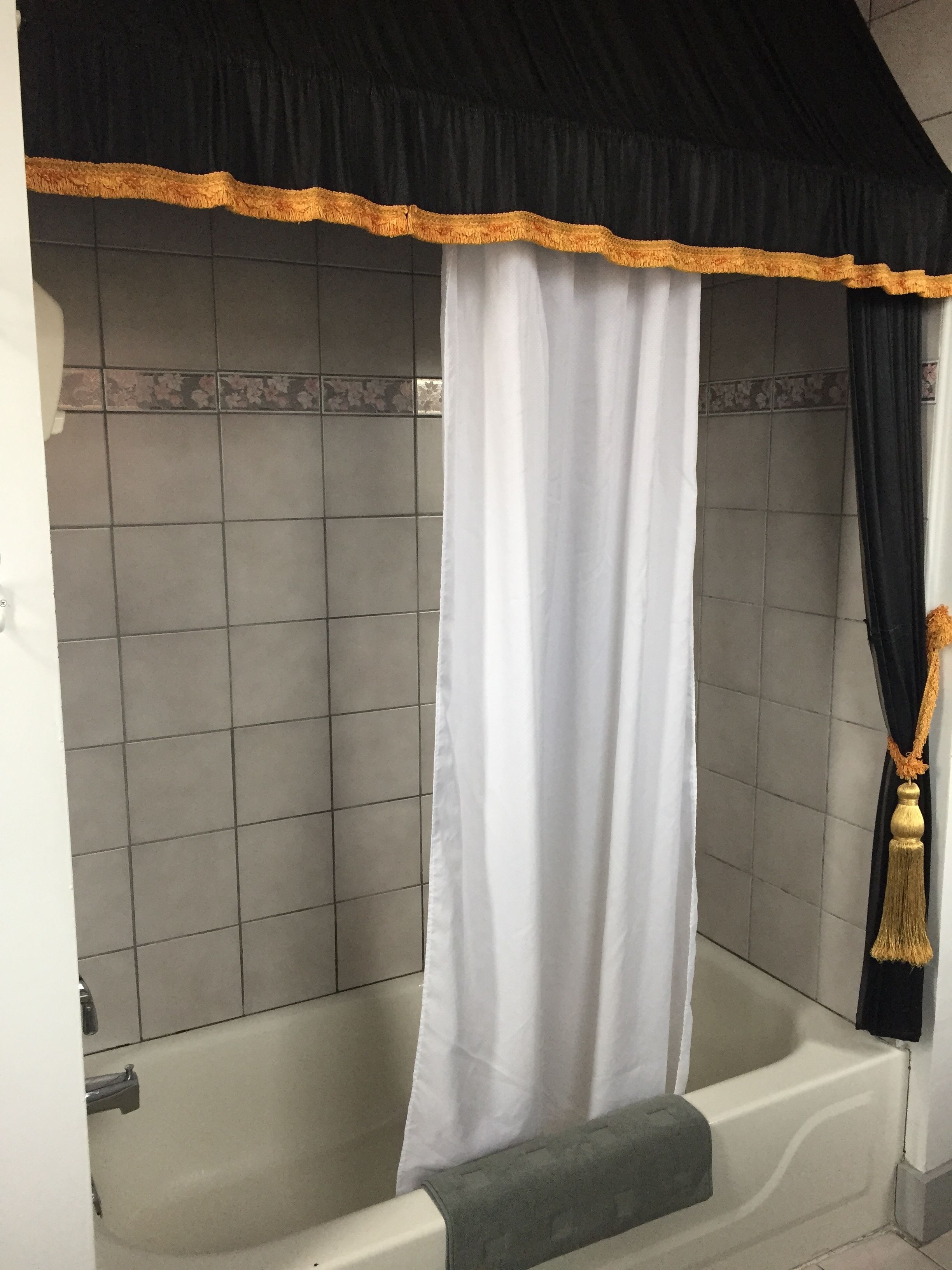 Ein Badezimmer mit einer Badewanne, einem weißen Duschvorhang und einem schwarzen und goldenen Zierstreifen.