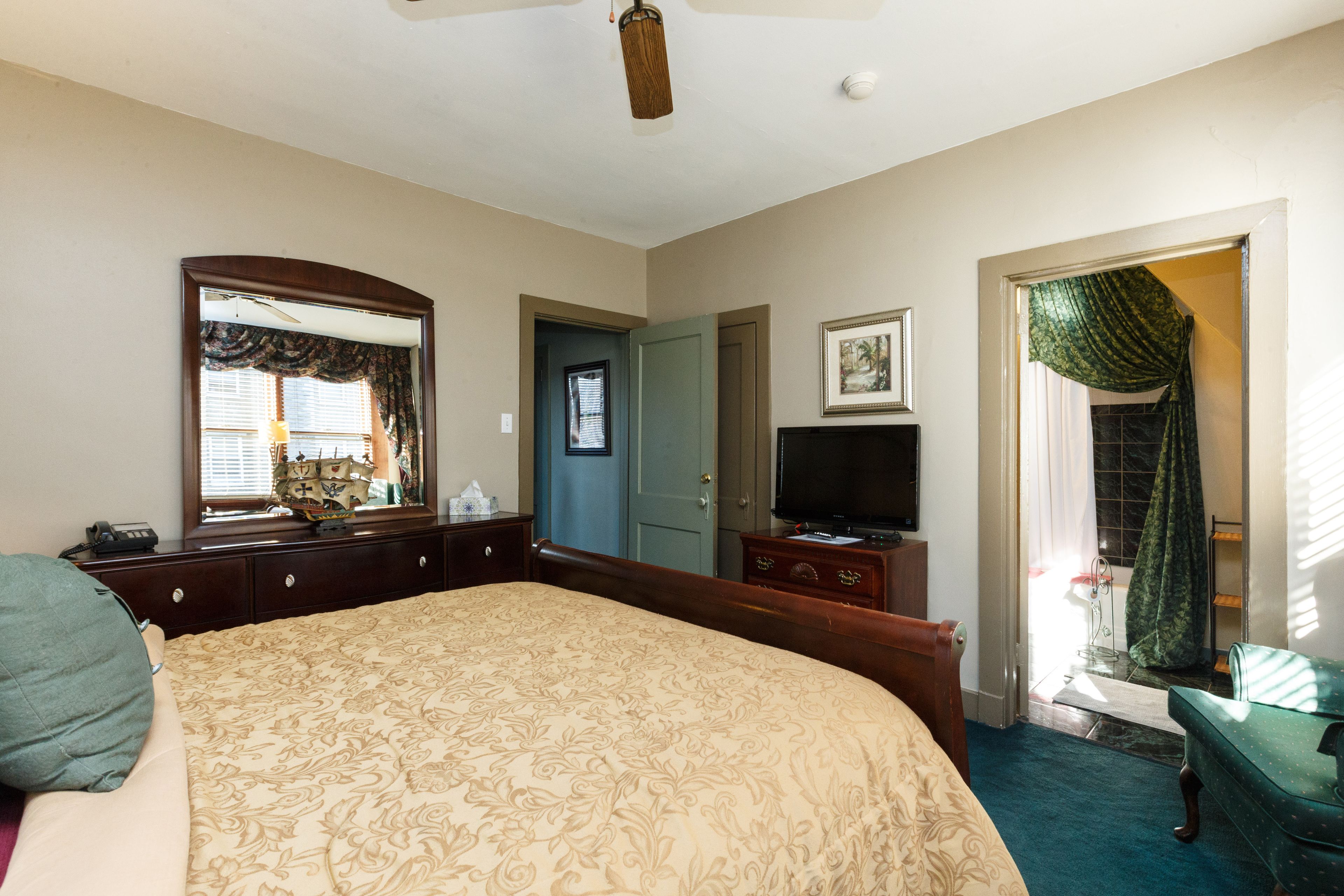 A bedroom with a large bed, a dresser, a television, and a door leading to another room.
