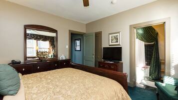 A bedroom with a large bed, a dresser, a television, and a door leading to another room.