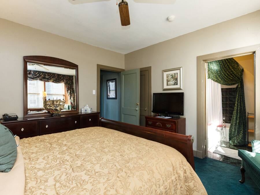 A bedroom with a large bed, a dresser, a television, and a door leading to another room.