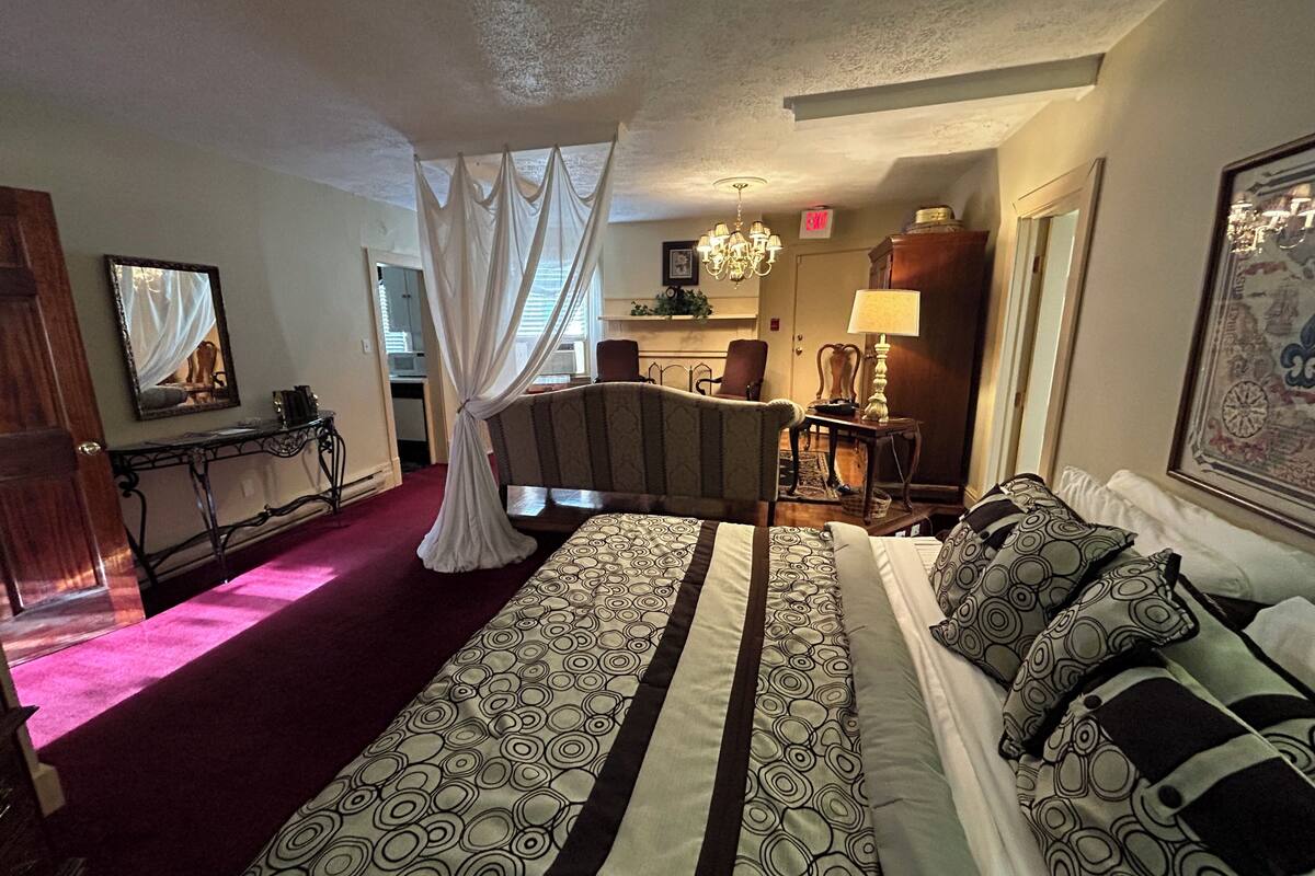 A hotel room with a large bed, a desk, a chair, a chandelier, and a painting on the wall.