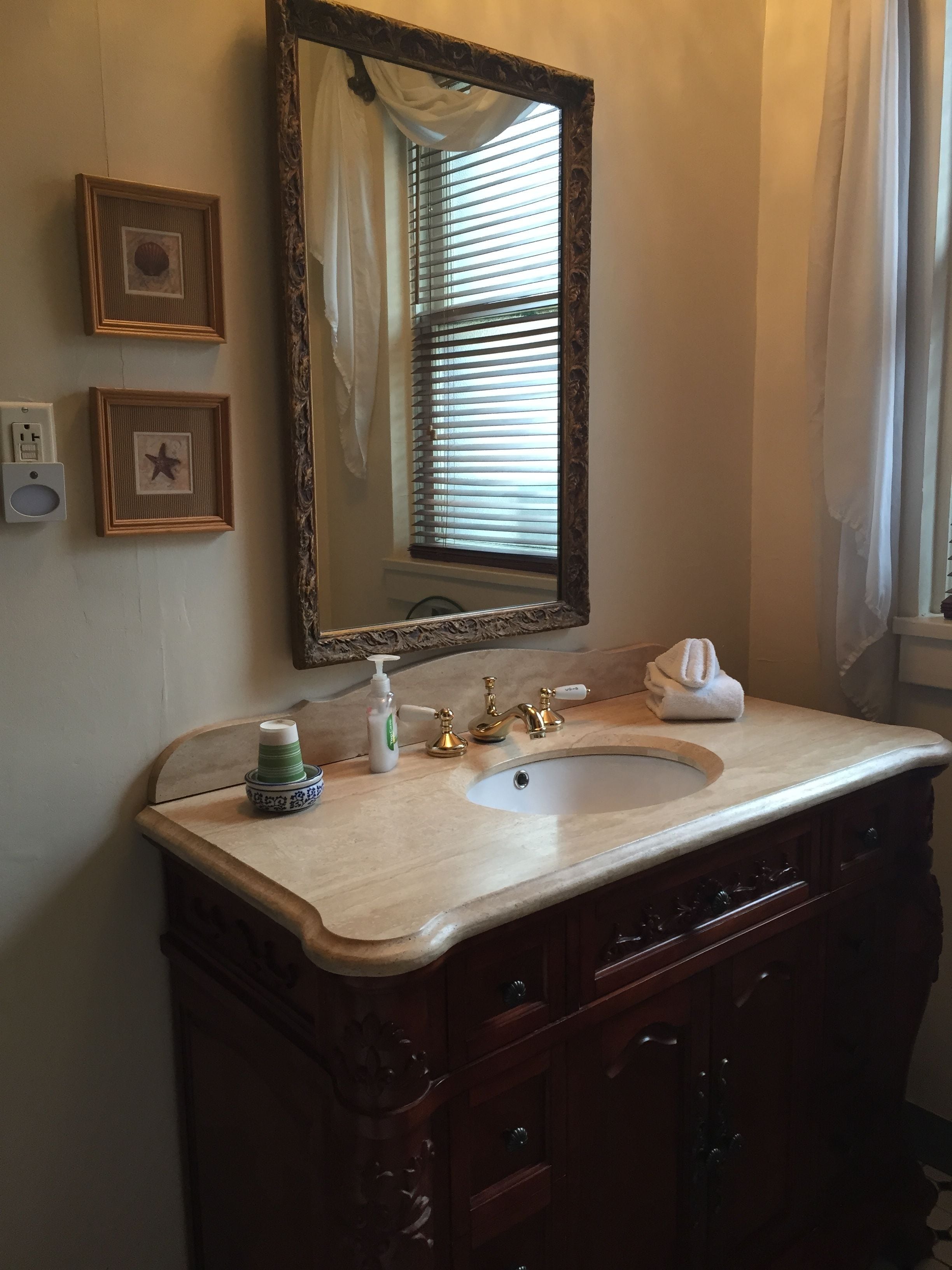 A bathroom with a large mirror, a sink with a marble countertop, and a wooden vanity with multiple drawers.