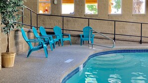 An indoor swimming pool with blue chairs and a potted plant. - Moose Creek Lodge & Suites (Cody)