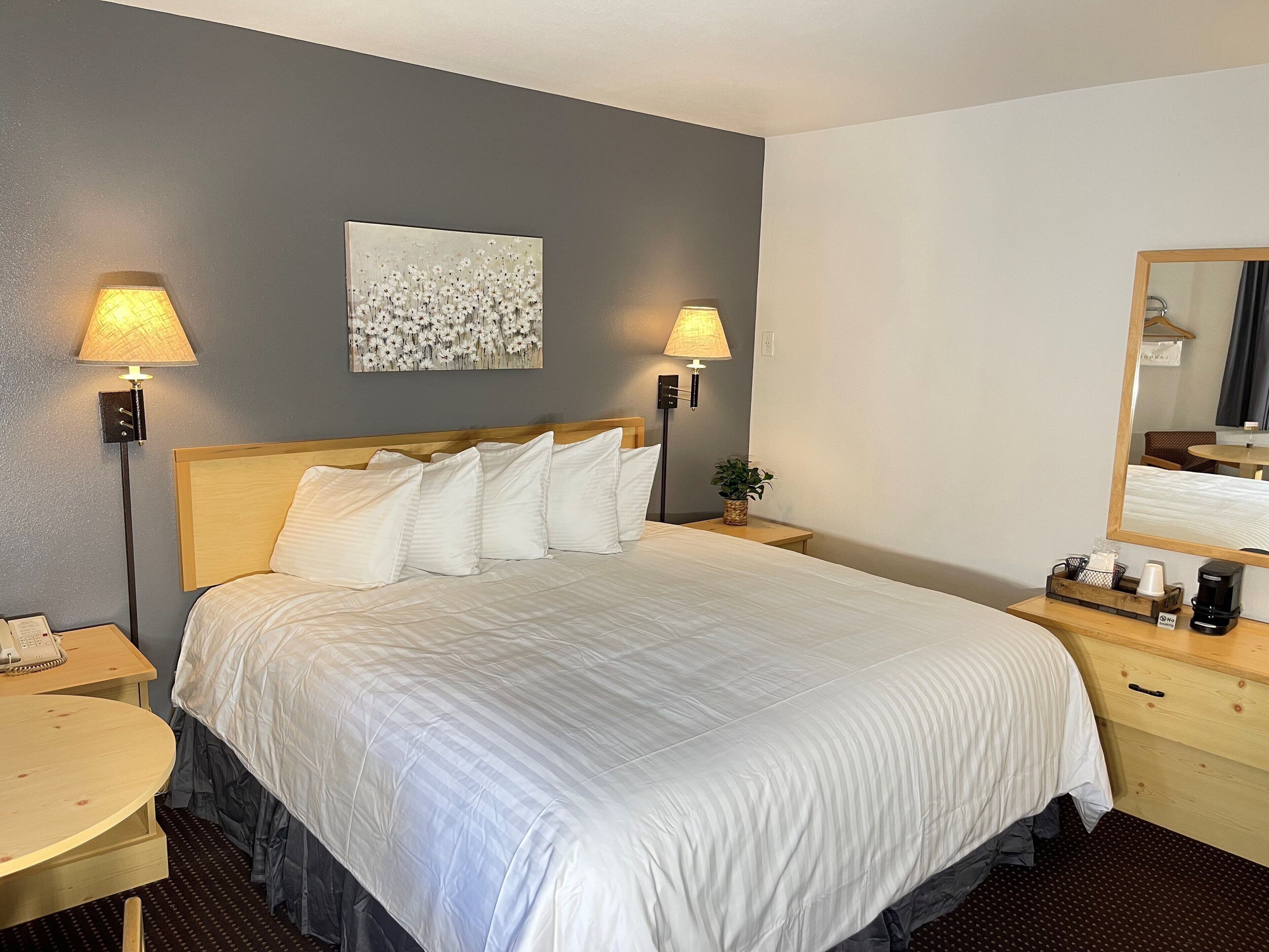 A neatly made bed with white linens, two bedside lamps, a small table with a phone, and a mirror on the wall.