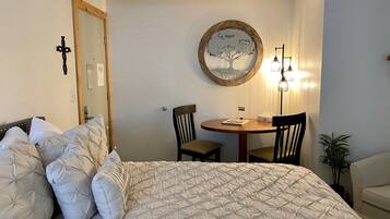 Ein Schlafzimmer mit einem Bett, einem runden Tisch mit Stühlen, einer Wandlampe und einem Spiegel.