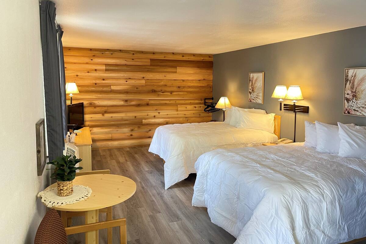 A hotel room with two beds, wooden panel walls, a round table with a plant, and two bedside lamps.