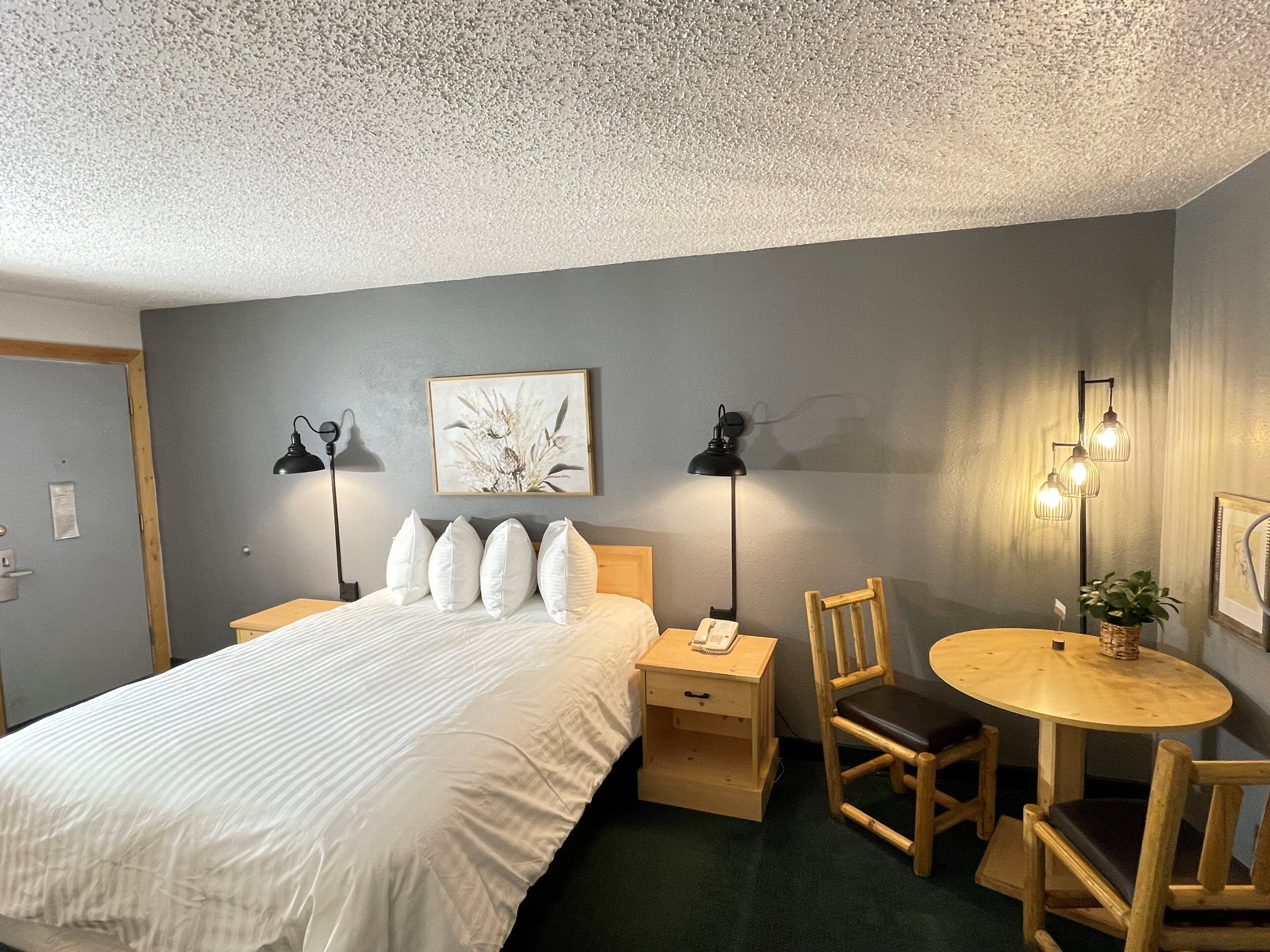 A neatly arranged bedroom with a bed, bedside lamps, a small wooden table, and a chair.