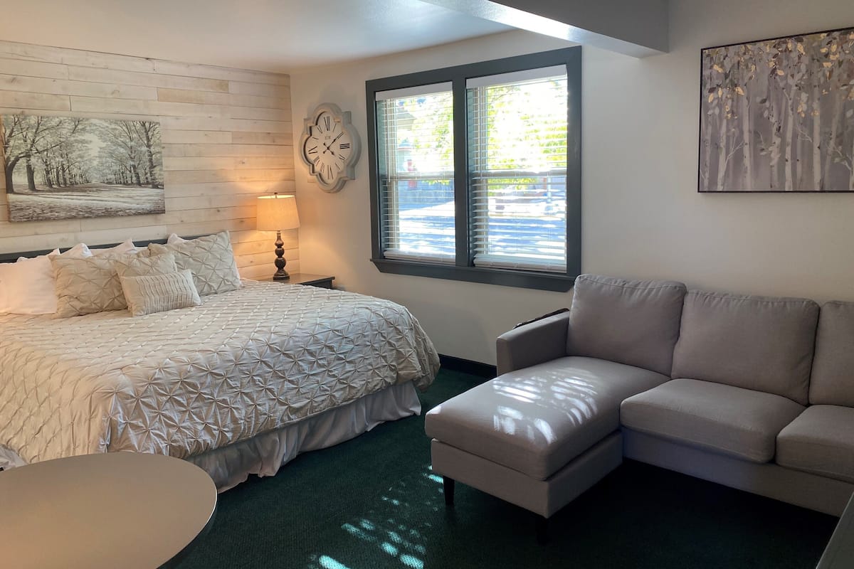 A bedroom with a bed, a nightstand, a lamp, a window with blinds, and a painting on the wall.