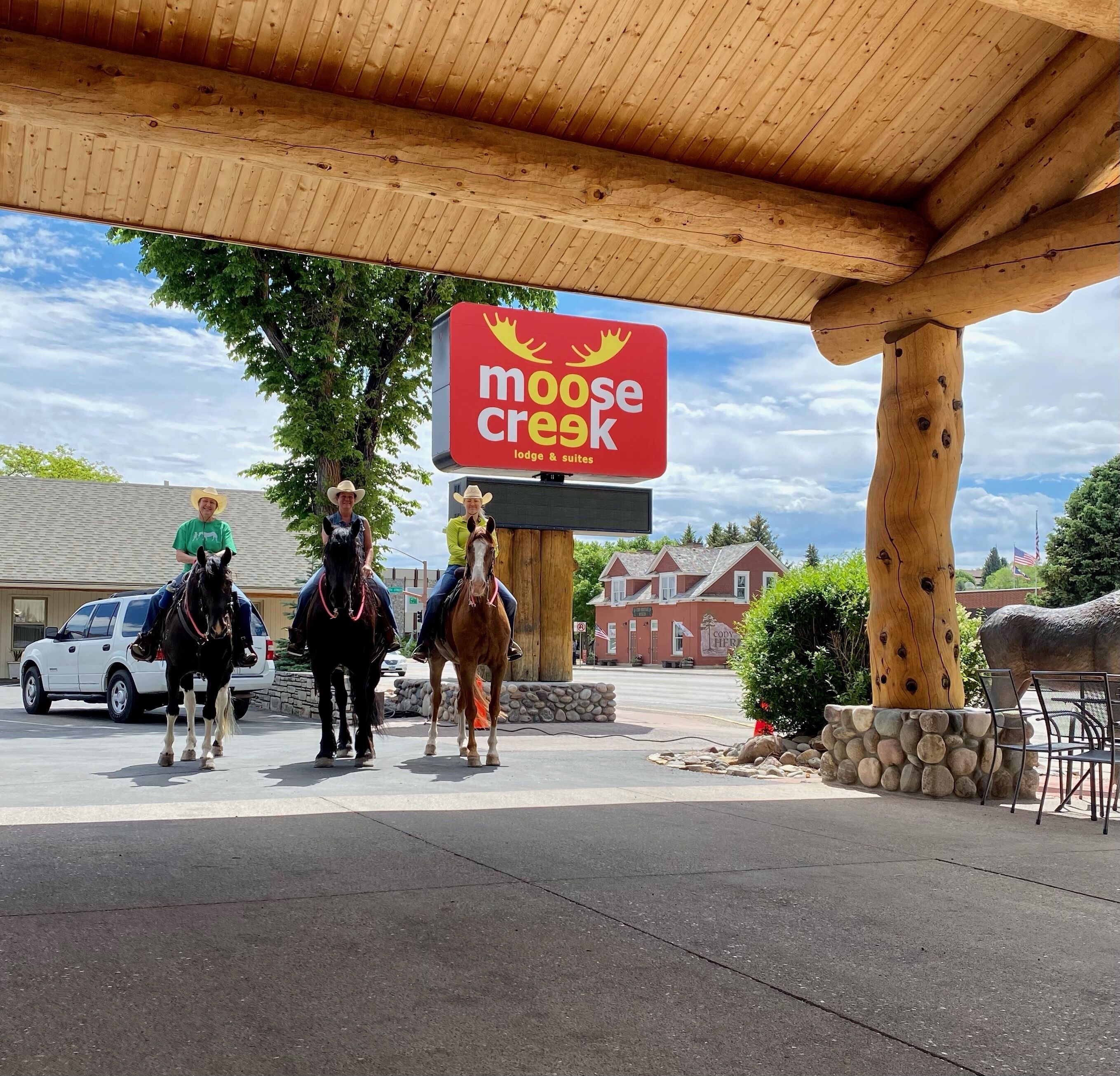 Letrero del Lodge & Suites Moose Creek, un estacionamiento techado y un carruaje tirado por caballos.
