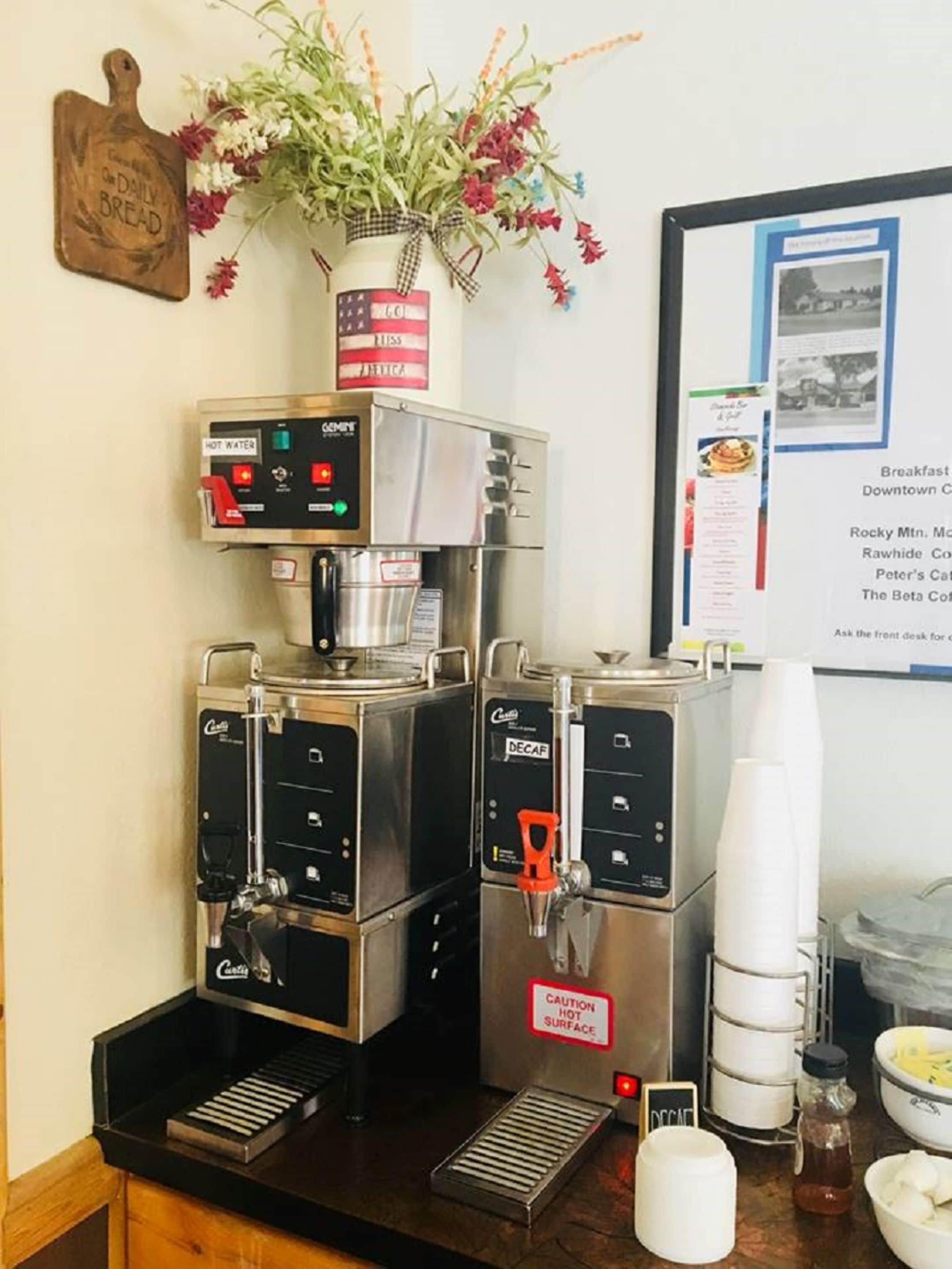 A coffee machine with multiple brewing options, a caution sign for hot surfaces, and a menu board in the background.