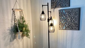 A room with a light grey sofa, a floor lamp with two light bulbs, a wall-mounted decorative panel, and a small table with a telephone. - Moose Creek Lodge & Suites (Cody)