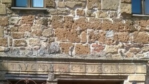 Un edificio de piedra con puerta de madera, una reja metálica y un pequeño ventanal con cortina.