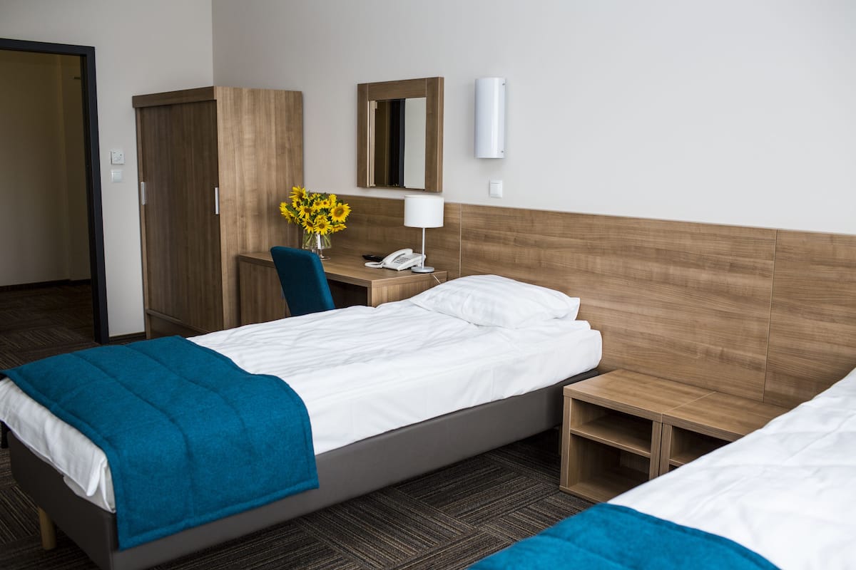 A hotel room with a bed, a desk with a phone, a mirror, and a small table with a vase of flowers.