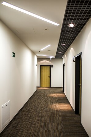 Un pasillo de hotel con pisos alfombrados, paredes blancas y una puerta de madera al final.