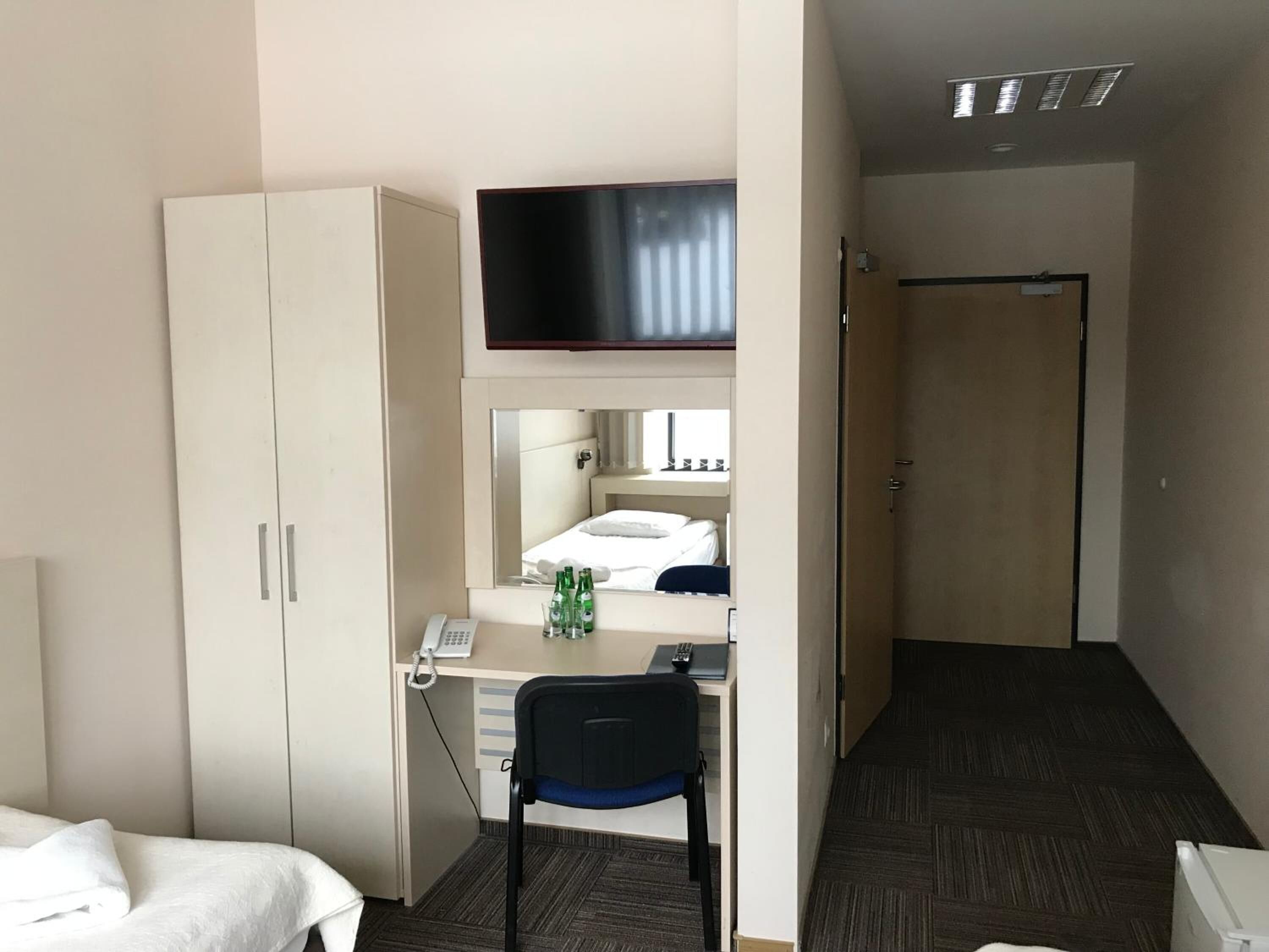 A hotel room with a bed, a desk with a telephone, a chair, and a television mounted above the desk.