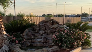 A landscaped area with a stone wall, pink flowers, and a palm tree.