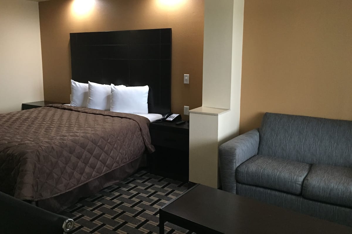 Ein Hotelzimmer mit einem Bett, einem Nachttisch, einem Telefon und einem grauen Sessel.