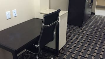 Una habitación de hotel con un escritorio negro, una silla de oficina negra, un armario blanco y un archivador negro.