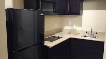 Una cocina compacta con un refrigerador negro, un microondas, un lavamanos y una estufa.