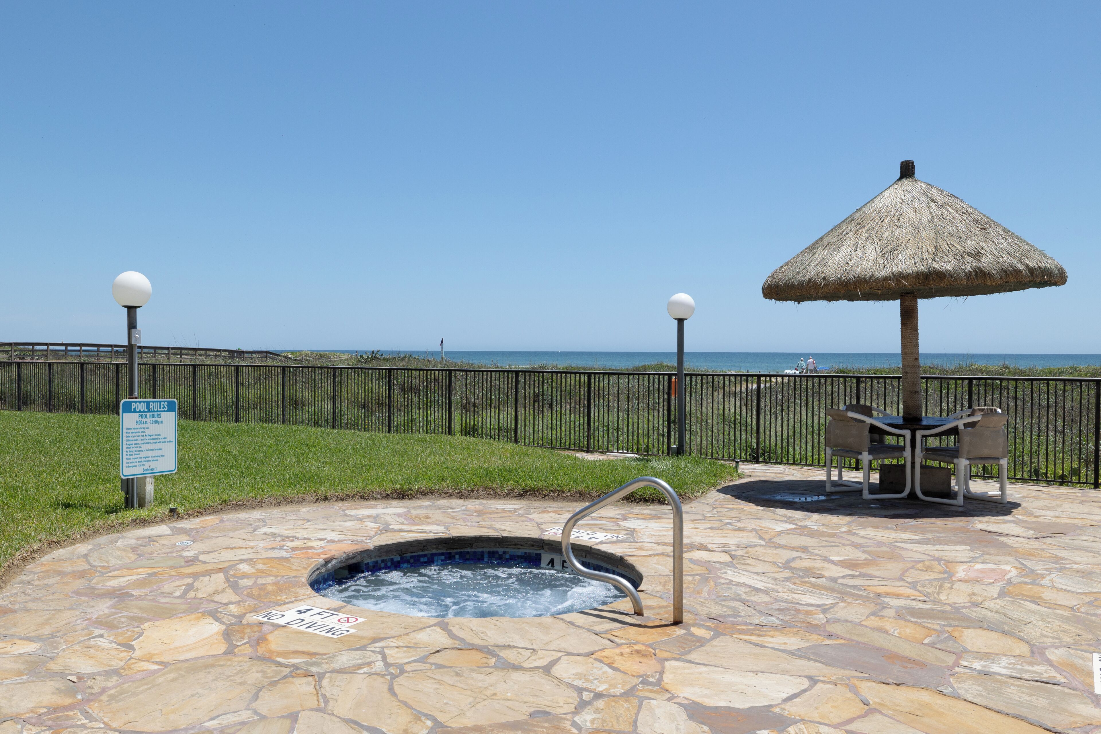 A stone pool with a hot tub, a thatched umbrella, and a sign indicating pool rules.
