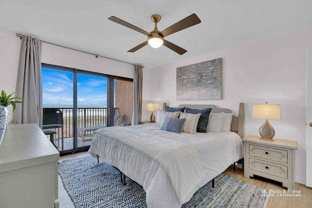 Un dormitorio con cama, mesitas de noche, ventilador de techo y vista a la playa.