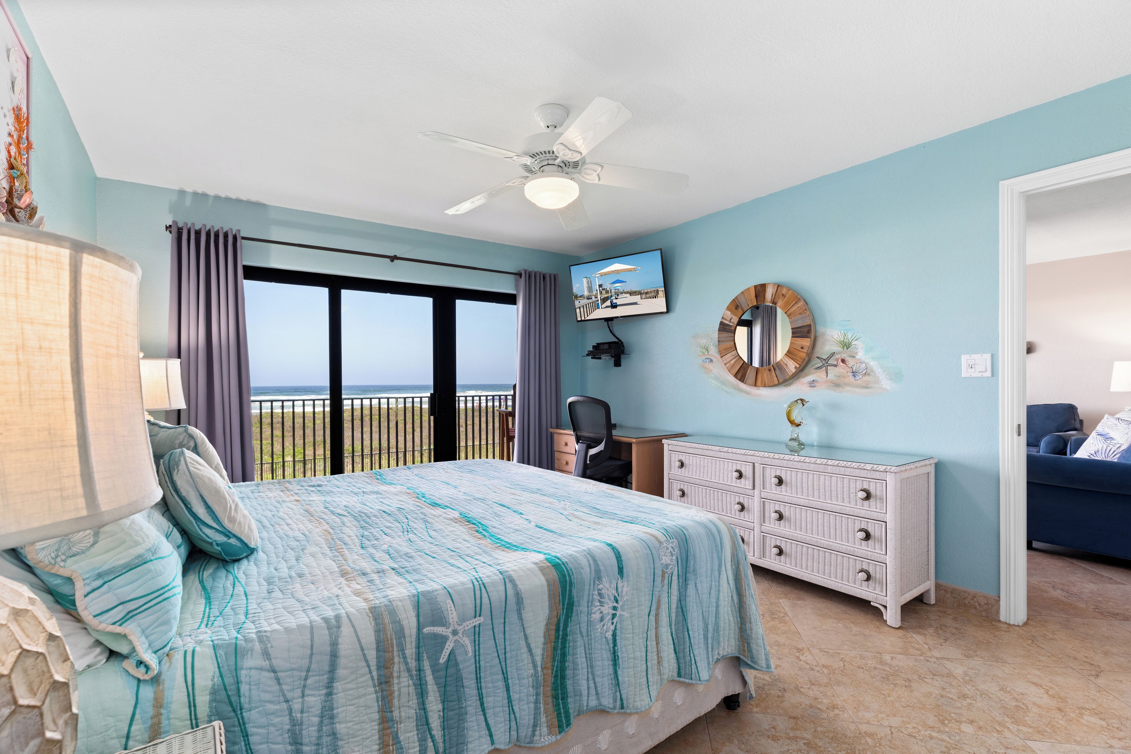 Una camera da letto con un letto, una scrivania, un comò, una ventola a soffitto e vista sull'oceano.