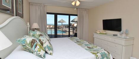 Habitación de hotel con cama, televisión, ventilador de techo y balcón con vista a la piscina.