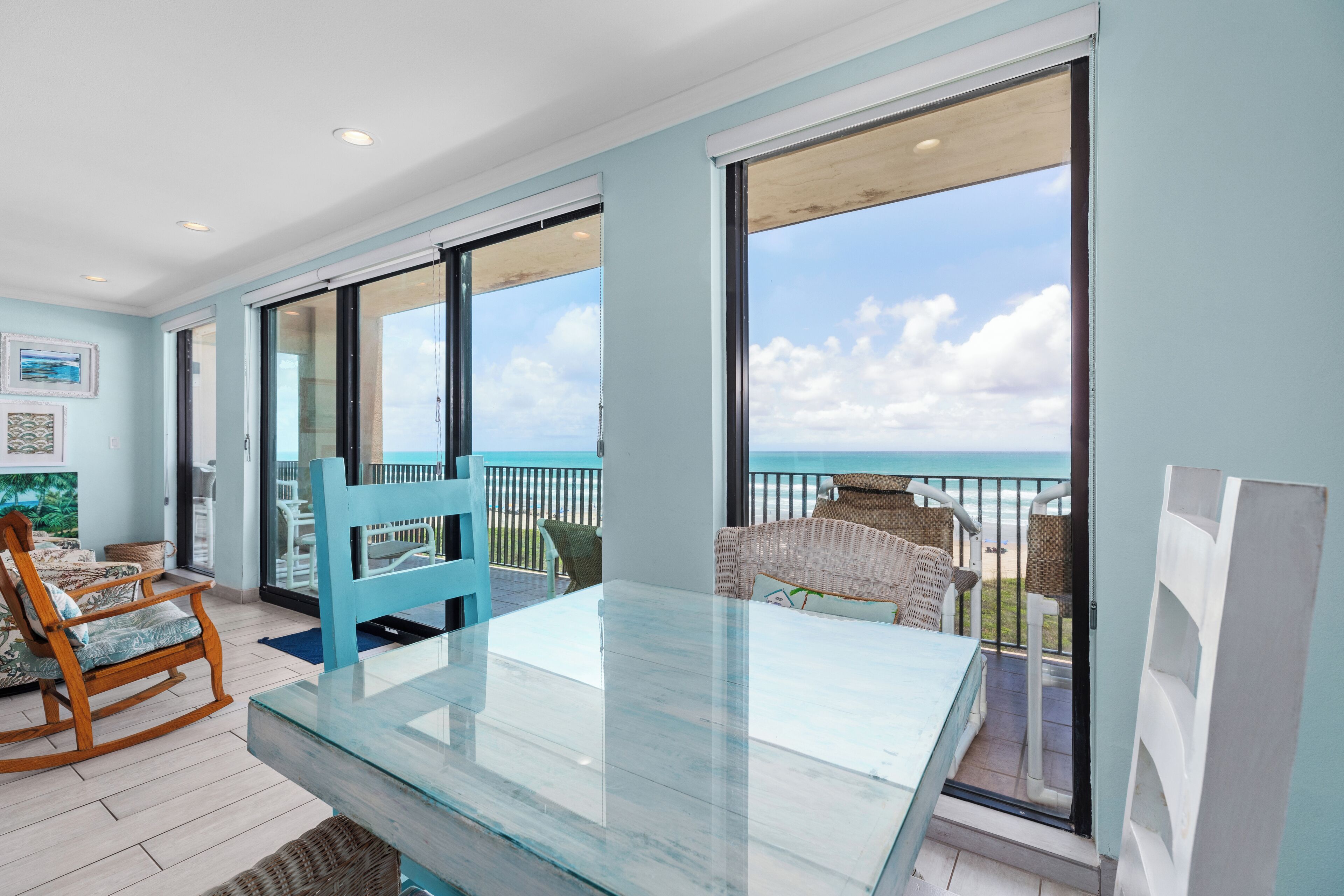 Ein geräumiger Balkon mit Glastisch und Stühlen, mit Blick auf einen Strand.