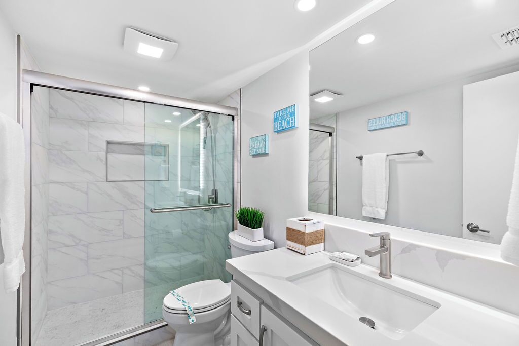Une salle de bain moderne avec une douche à parois de verre, des toilettes blanches et un grand miroir au-dessus du lavabo.
