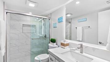 Une salle de bain moderne avec une douche à parois de verre, des toilettes blanches et un grand miroir au-dessus du lavabo.